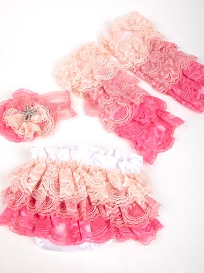 A complete baby girl's outfit with a pink and peach ruffled lace bottom, matching leg warmers, and a headband.