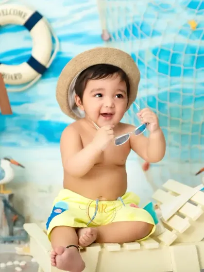 A perfect 'Beach Baby' theme, with this little one wearing a hat and sunglasses while sitting on a miniature beach chair. The set includes a nautical backdrop, a windmill, and seagulls.