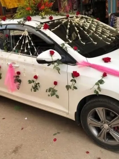 A simple and sweet car decoration with single red roses, a pink ribbon, and strings of white flowers on the side.