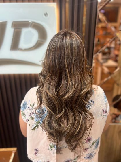 A beautiful balayage with soft waves. The color is concentrated towards the ends for a natural, sun-kissed effect, shown here against our salon's signature backdrop.