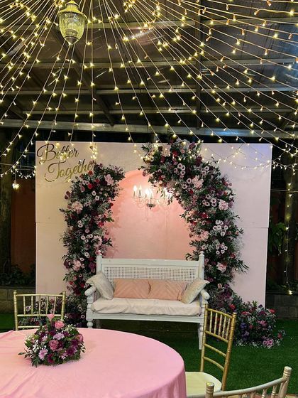 A romantic 'Better Together' setup perfect for an engagement or anniversary. The soft pink backdrop, floral arch, and twinkling fairy lights create a dreamy and intimate atmosphere.