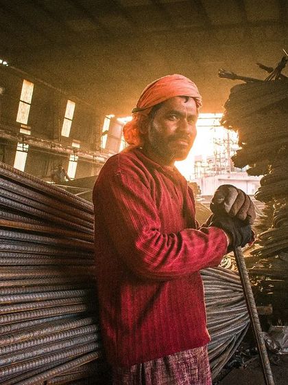Here is another shot of the worker at the steel yard. In this frame, I stepped back a bit to show more of the stacked iron rods, emphasizing the industrial environment he works in.