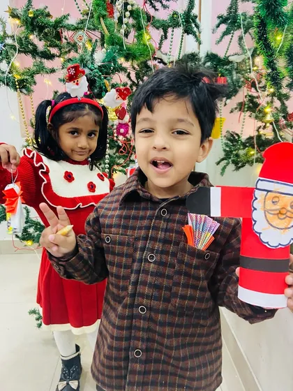 Two friends posing with their handmade Santa Claus crafts in front of the Christmas tree.