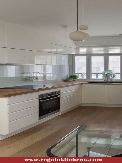 A minimalist parallel kitchen with white handle-less cabinets and a light wood countertop. The large windows at the end of the galley fill the space with natural light, enhancing the clean and airy feel.