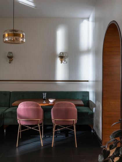 Color and texture play a huge role in atmosphere. Here, plush pink chairs contrast beautifully with a deep green velvet booth. The fluted wall paneling and warm lighting create a sophisticated and inviting dining spot.