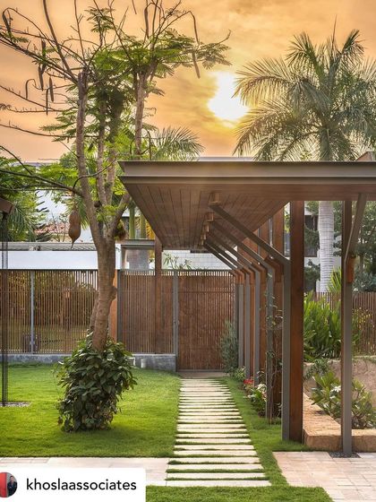 A stone pathway leading through a garden towards a wooden pergola at sunset. The warm light and long shadows create a magical and inviting atmosphere, showcasing the importance of lighting in landscape design.