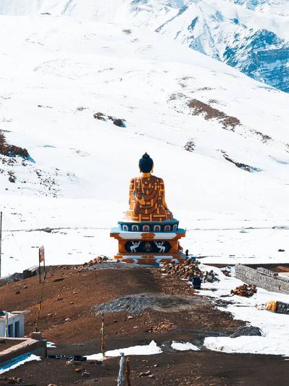The magnificent Buddha statue in Spiti, standing as a symbol of peace against a backdrop of pristine snow. This shot combines spiritual iconography with the raw beauty of the Himalayan landscape.
