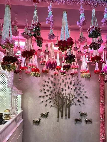 A beautiful home corner transformed for a wedding celebration. The ceiling is adorned with intricate hanging floral arrangements in shades of pink, while a metallic tree-of-life wall art adds a modern touch.