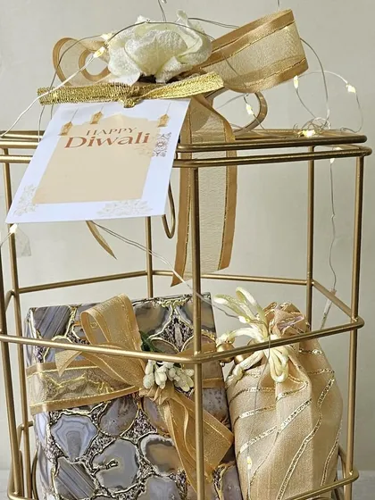 A close-up of a golden birdcage hamper, beautifully wrapped and ready for gifting. It contains agate-print boxes and a delicate potli, making it a stylish and sophisticated Diwali present.
