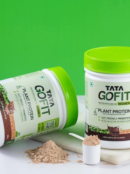 A clean product shot for Tata GoFit, featuring two tubs and a scoop of powder. The bright green background reinforces the brand's energetic and healthy identity.