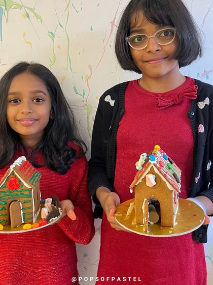 Two sisters proudly hold up their finished gingerbread creations, ready to be displayed for the holidays.