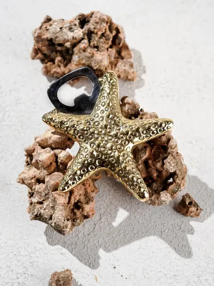 A unique product shot of a starfish-shaped bottle opener, styled with a rock to create a beachy, summer vibe.