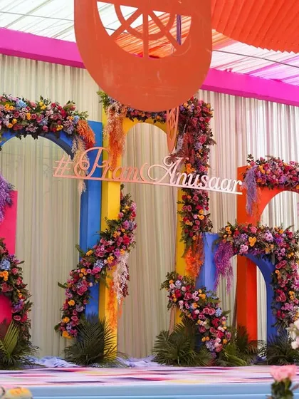 Another angle of the Haldi stage, showing the layered arches and the lush floral arrangements that seem to grow organically over them. The custom hashtag for the couple is subtly placed in the center.