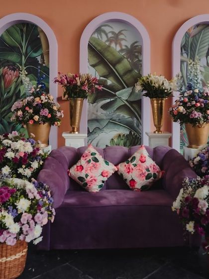 A plush purple sofa serves as a photo booth, surrounded by vibrant floral arrangements.