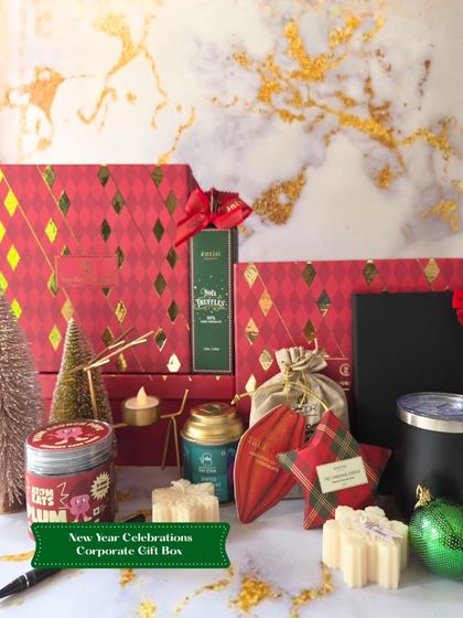 A festive flat-lay of the New Year Celebrations Corporate Gift Box. This image shows the red and gold themed box along with some of the contents like plum crunch pops and a travel tumbler.