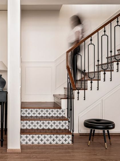 The staircase at 'Riviera Maison' is a masterpiece of custom design. The risers are adorned with black and white tiles, and the wrought iron balusters feature a unique, decorative pattern, turning a functional element into a work of art.