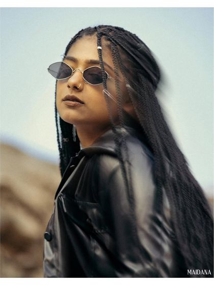 A close-up portrait with a slight motion blur effect on the model's braids. Her cool demeanor and stylish sunglasses make this a compelling shot for a fashion or accessory brand.