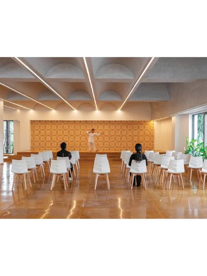 The multi-purpose hall in the 'Meraki' clubhouse features a vaulted ceiling with integrated lighting and a patterned tile backdrop, creating a flexible and elegant space for events.