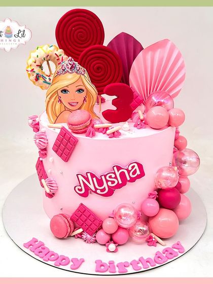 A dreamy pink Barbie cake for Nysha's 3rd birthday, loaded with pink spheres, macarons, and lollipops for a true candy-glam vibe.