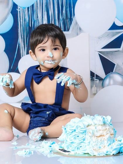 Caught with a bit of frosting on his face, this little one looks right at the camera. It's a charming and funny portrait from his blue-themed first birthday.