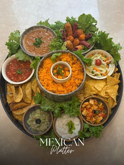 A vibrant Mexican Platter featuring spicy rice, nachos, guacamole, salsa, and other delicious dips and bites, all arranged on a bed of fresh lettuce.