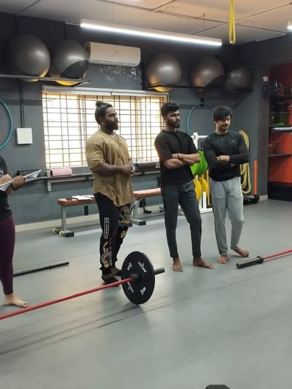 A student practices his barbell technique under the watchful eye of a trainer and fellow students. This peer learning and expert feedback environment accelerates skill development.