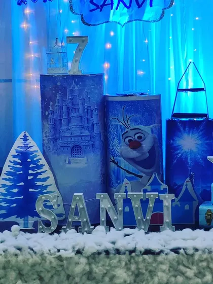 Detailed props for a Frozen-themed party, including character-printed pedestals, a faux snow-covered table, and light-up letters.