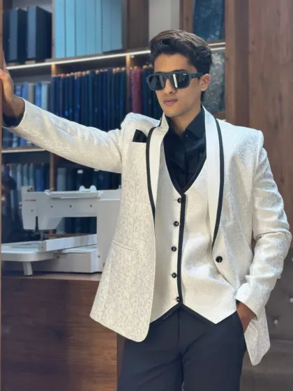 A stunning white three-piece tuxedo with black lapel detailing. This high-contrast look is perfect for grooms who want a modern yet timeless outfit for their wedding day.