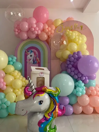 A whimsical unicorn birthday setup with a large unicorn head foil balloon as the centerpiece. The decoration uses soft pastel balloons and a rainbow backdrop to create a dreamy atmosphere.