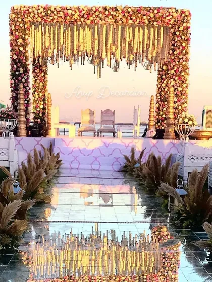 A picture of pure elegance. This seaside mandap, framed with lush florals and pampas grass, features a stunning mirror aisle that reflects the sky, creating a truly magical setting for your vows.