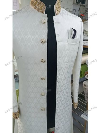 This is a closer view of a white wedding sherwani, highlighting the rich fabric and the detailed zardosi work on the collar and cuffs. The buttons are carefully chosen to complement the gold embroidery, ensuring a cohesive and polished look.