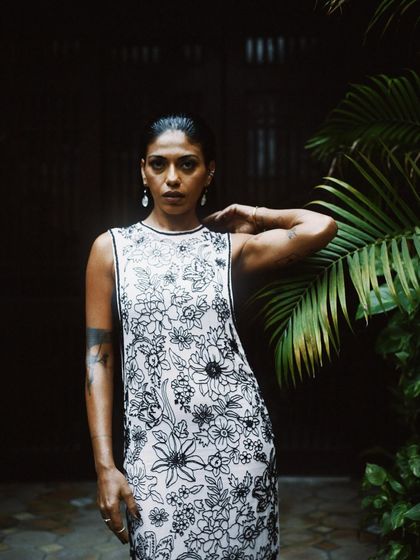 A striking portrait of Anasuya Sengupta against a backdrop of lush greenery. Her direct gaze is powerful and engaging.