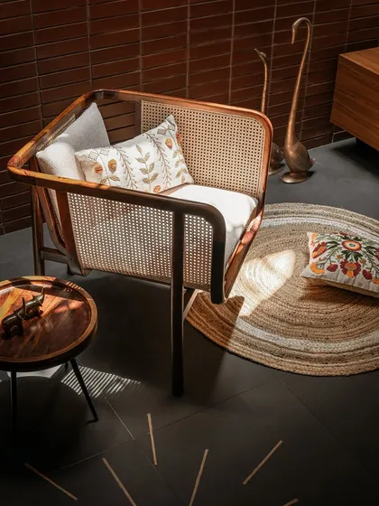The elegant lines of this modern cane armchair are highlighted by the dramatic play of light and shadow against the dark floor and brick wall.