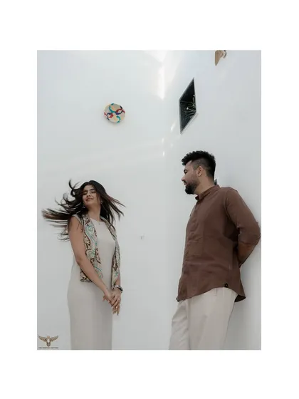 A modern portrait against a minimalist white wall, where the focus is entirely on the couple's interaction. The motion in her hair adds a dynamic, candid feel to this stylish shot.