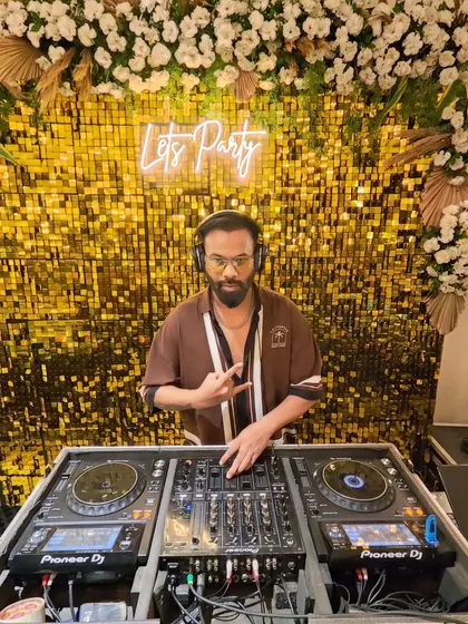 My DJ booth set up in front of a 'Let's Party' neon sign and a shimmering gold backdrop. This is a popular setup for cocktail parties and sangeets.