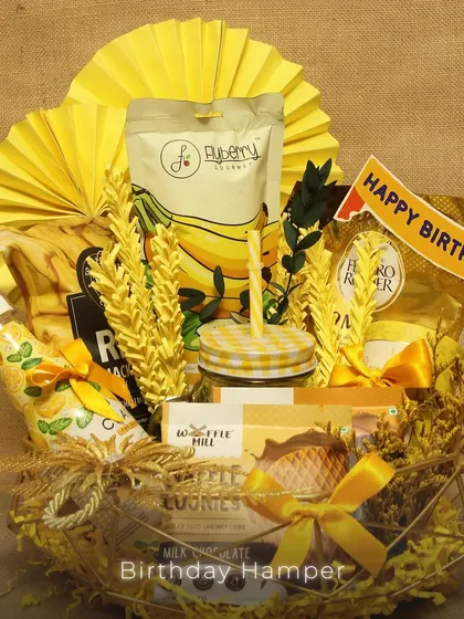 A cheerful, yellow-themed birthday hamper. This basket is filled with banana-flavored treats, a mason jar, waffle cookies, and a 'Happy Birthday' banner, creating a sunny and joyful gift.