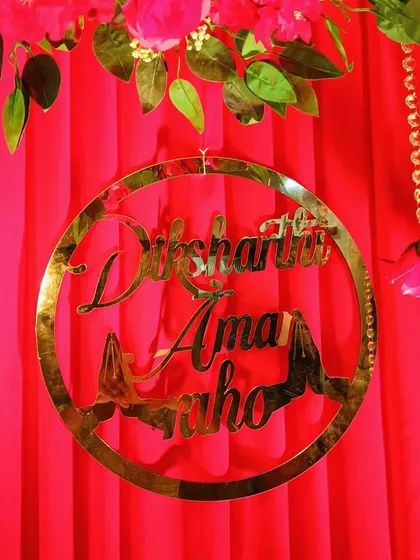 A custom gold acrylic hoop with a Jain blessing, "Diksha Tapasvi Amar Raho," adds a personal and cultural touch to the elegant red decor.