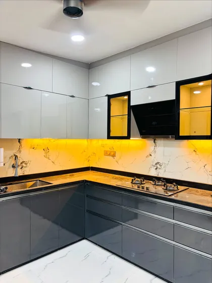 A look at a modern L-shaped kitchen I designed, featuring high-gloss grey and white cabinets for a sleek look. The design includes a marble-patterned backsplash and warm under-cabinet lighting, making the space both functional for cooking and aesthetically pleasing.