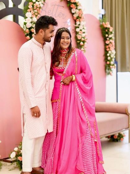 A full-length view of the happy couple. The vibrant pink of the bride's outfit and the groom's matching kurta create a perfect picture for any wedding event.