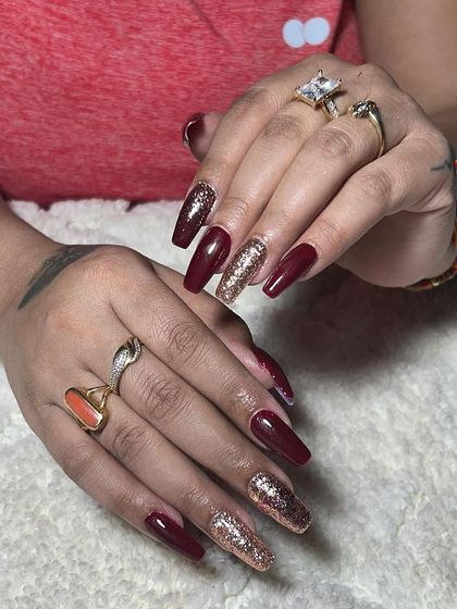 A dramatic, long coffin set with deep red and rose gold glitter nails. This is a bold and glamorous statement.