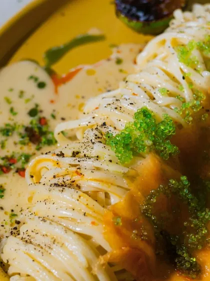A close-up of the Linguine with Salmon Carpaccio, showing the vibrant green tobiko and creamy yuzu butter sauce. It's a dish that's as beautiful as it is delicious.