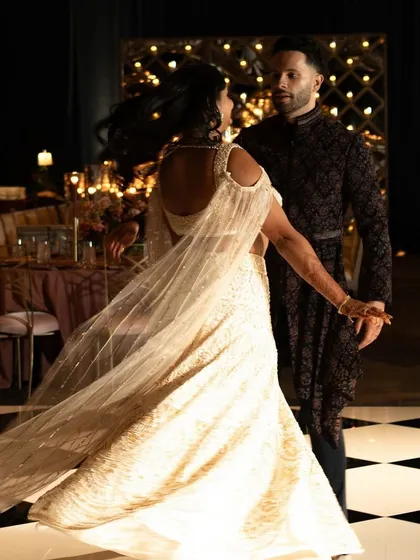 A reception look that is all about modern glamour. The bride's shimmering ivory lehenga and the groom's dark, textured sherwani create a stunning contrast on the checkered dance floor.