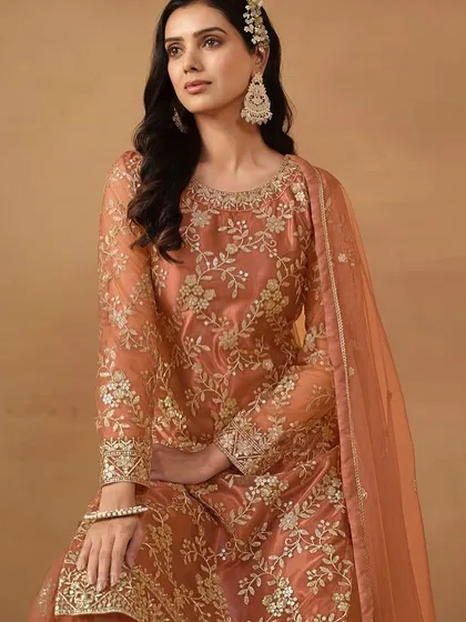A beautiful dark salmon net suit with sharara pants. The delicate sequence work gives it a soft shimmer, perfect for a daytime wedding or festive gathering.
