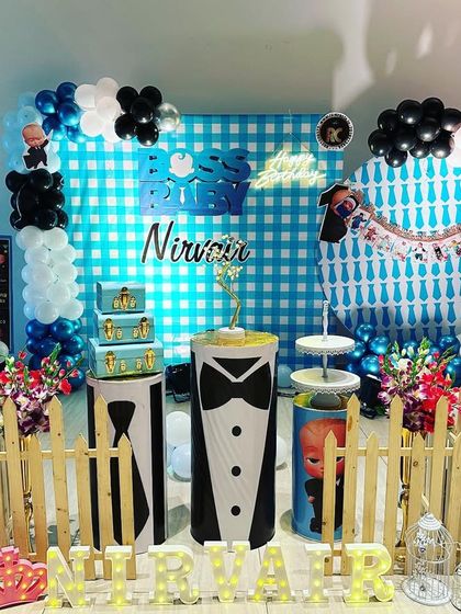 A full Boss Baby setup with multiple character cutouts and themed plinths. The blue gingham backdrop and balloon columns complete the look.