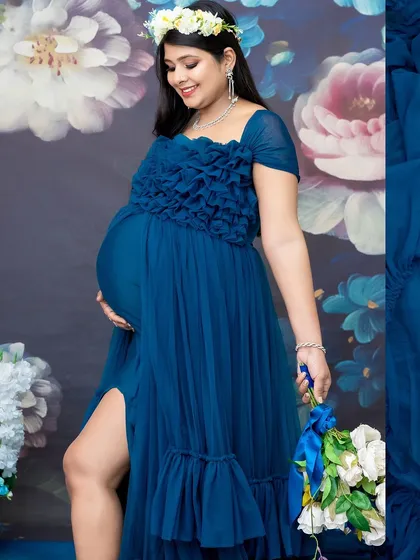 A close-up shot showcasing the details of the gown and the beauty of the baby bump. The floral backdrop adds a touch of romance to this elegant portrait.