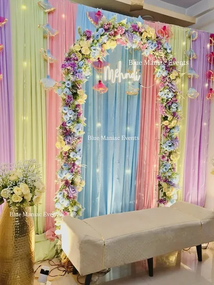 The full view of the pastel Mehendi backdrop. The multi-colored pastel drapes, floral arch, and golden vases create a dreamy and whimsical setting for your ceremony.