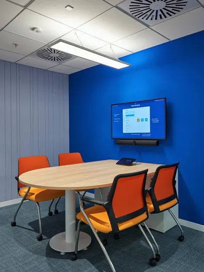 A simple and effective meeting room with a bold blue accent wall and contrasting orange chairs. This setup is perfect for small team meetings.