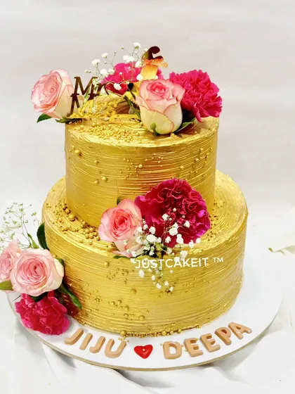 A stunning all-gold two-tier reception cake. The metallic finish is beautifully complemented by fresh pink and red flowers, creating a look of pure luxury.