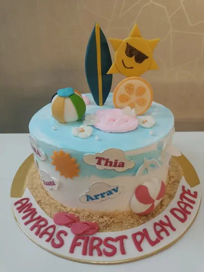 A fun beach-themed cake for a "first play date." It’s decorated with edible sand, a surfboard, and other sunny-day elements.