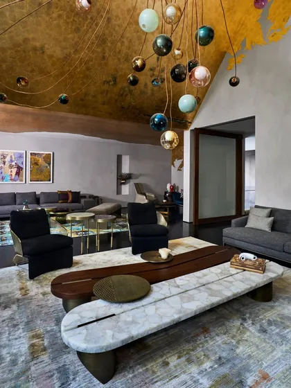 The grand living room at the Baid Residence, with its double-height ceiling adorned with gold leaf and a Bocci light installation. The space is furnished with pieces from Minotti and Poliform, creating a luxurious yet inviting environment.